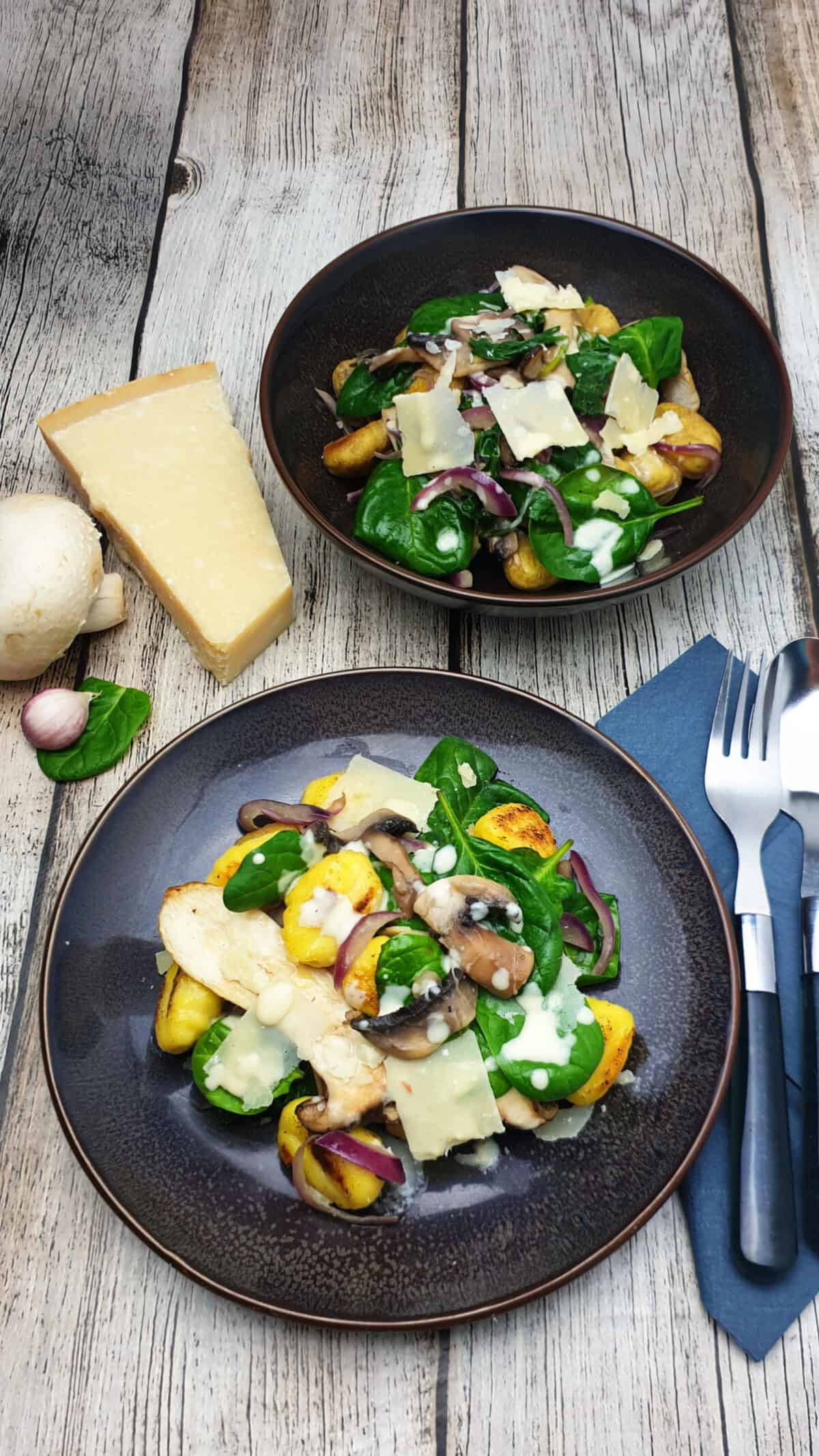 Auf einem braunen Teller angerichtet ein Gnocchi Salat mit Spinat. Im Hintergrund Deko.