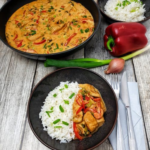 Puten-Curry mit Gemüse in einer braunen Schale mit Reis serviert und mit Frühlingszwiebeln bestreut.