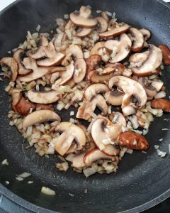 In einer Pfanne angedünstete Pilze mit Zwiebeln in Öl.