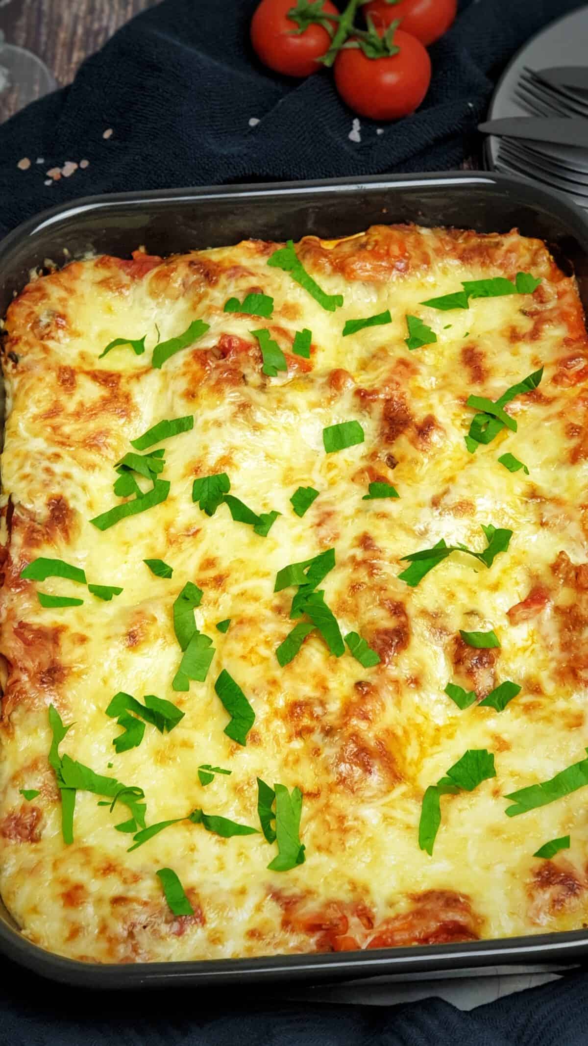 In einer dunklen Auflaufform eine Gemüse-Lasagne mit Käse überbacken. Im Hintergrund Deko.