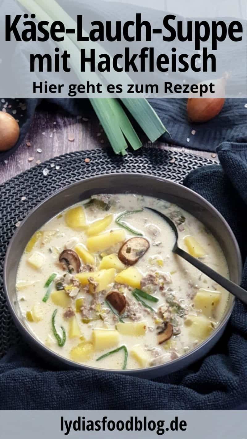 Eine graue Suppenschale mit einem Esslöffel gefüllt mit einer Käse-Lauch-Suppe. Im Hintergrund sieht man eine Stange Lauch, eine Zwiebel und Champignons, dekorativ auf einem Küchenhandtuch fotografiert.