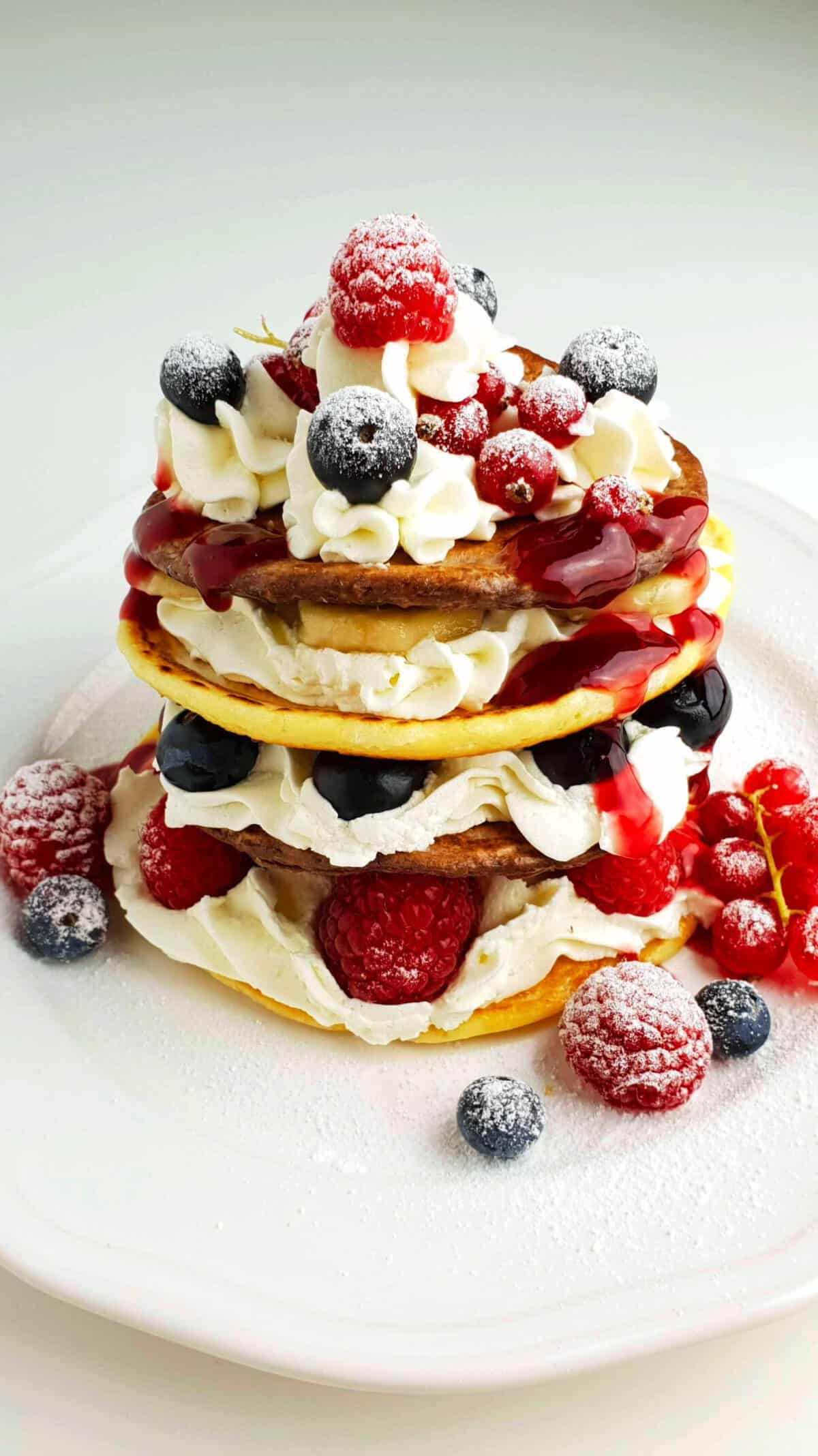 Auf einem weißen Teller Pancakes mit Sahne und frischen Früchten.