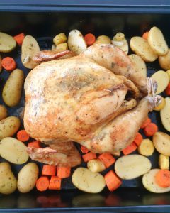 Eine gefüllte und marinierte Poularde/Ganzes Hähnchen mit Kartoffeln und Möhren Gemüse auf einem Backblech.