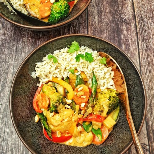 Gemüse-Curry mit Blumenkohl und Brokkoli mit Kokosmilch serviert mit Reis in einer braunen Schale.