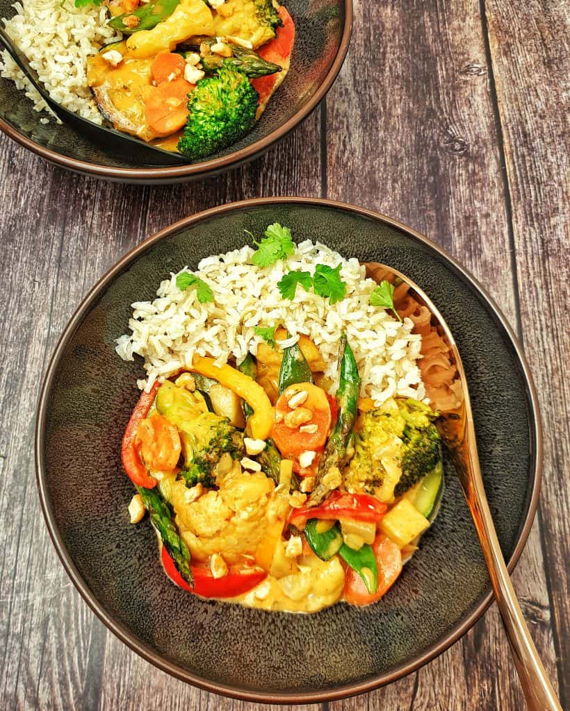 Gemüse-Curry mit Blumenkohl und Brokkoli mit Kokosmilch serviert mit Reis in einer braunen Schale.