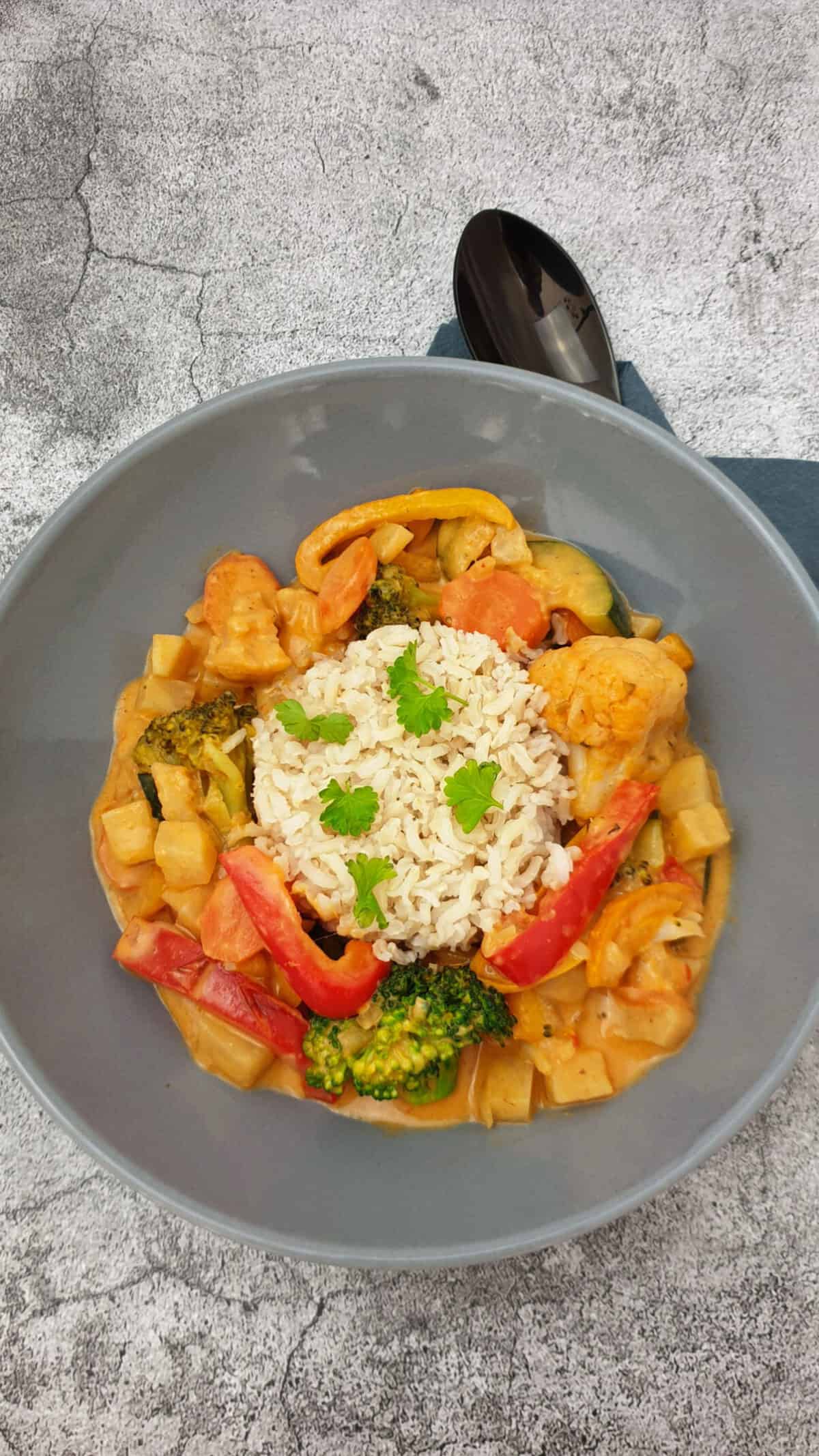 Gemüse Curry mit Blumenkohl und Brokkoli in einer grauen Schale mit Reis serviert.