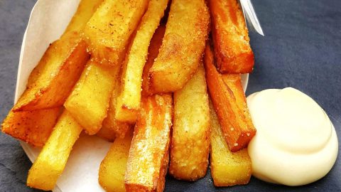 Selbst gemachte 2erlei Pommes aus Kartoffel und Süßkartoffel in einer Papiertüte mit Mayonnaise auf einer Schieferplatte serviert.
