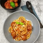 Italinische Hackbällchen mit Spaghetti angerichtet in einer grauen Schale mit Parmesan und Basilikum garniert.