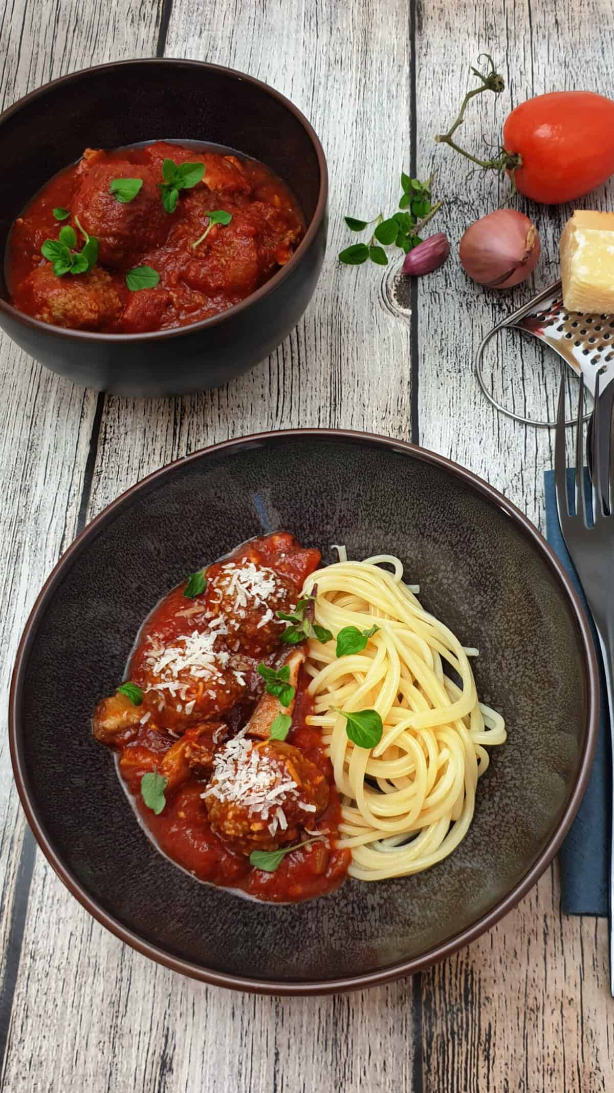 Italienische Hackbällchen mit Spaghetti in einer braunen Schale angerichtet. Mit Parmesan bestreut.