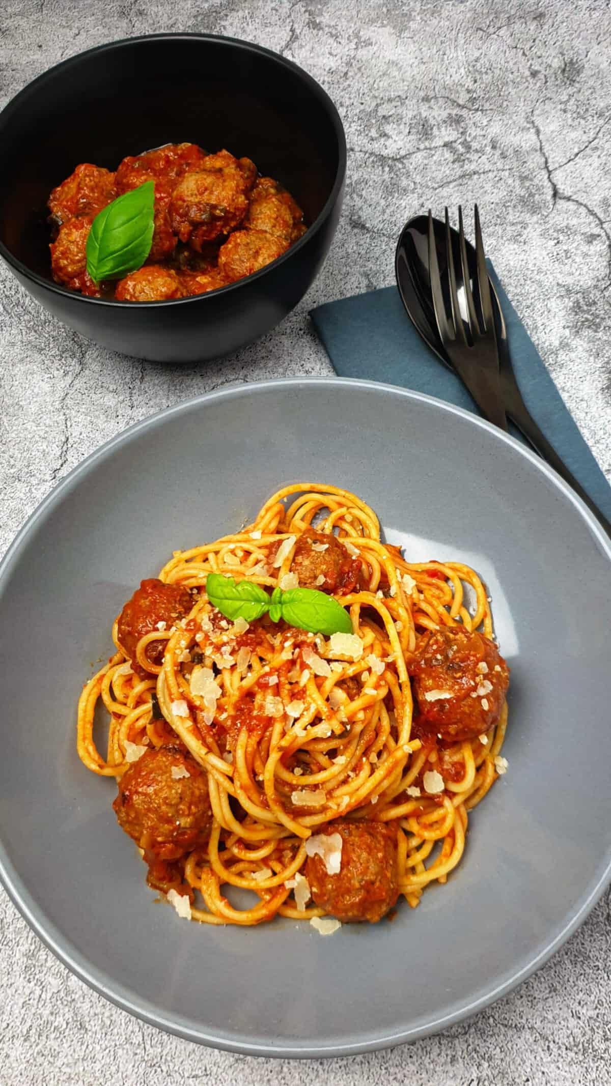Italienische Hackbällchen mit Spaghetti in einer braunen Schale angerichtet. Mit Parmesan bestreut.