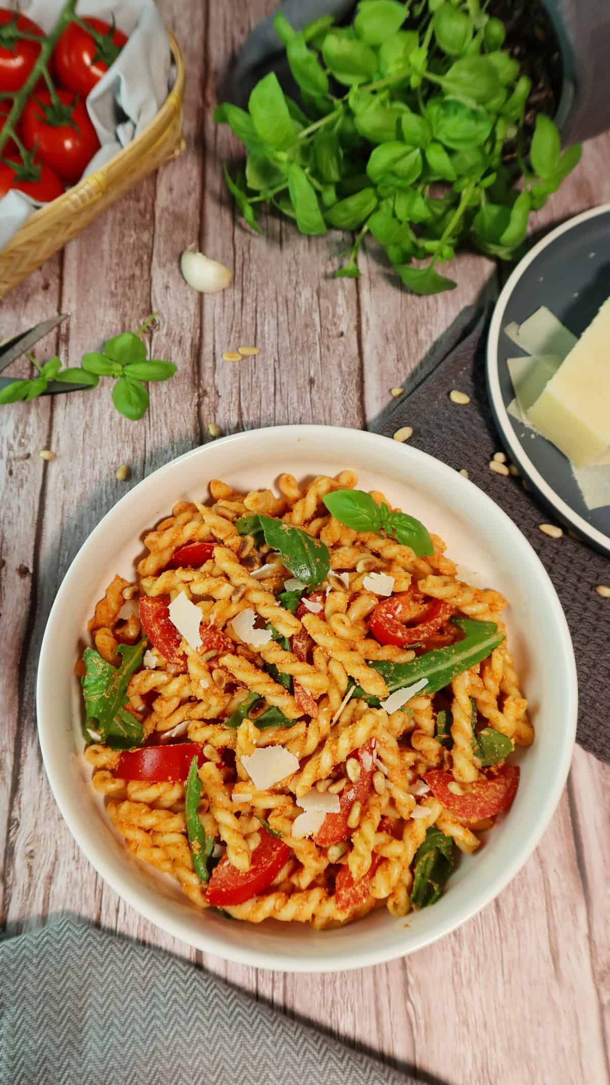 In einer weißen Schale ein italienischer Nudelsalat mit Tomate, Rucola und rotem Pesto. 
