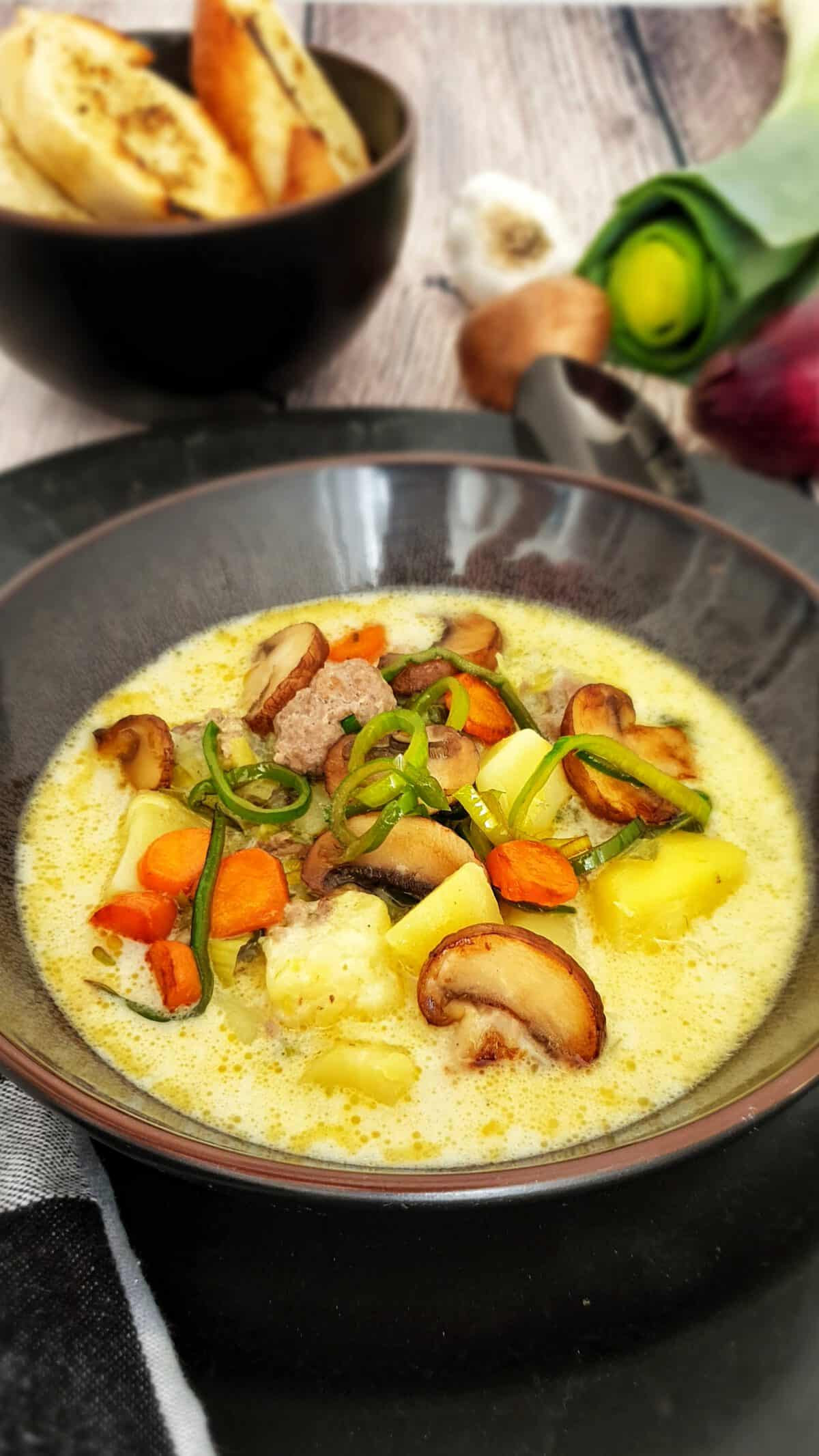 Käse-Lauch-Suppe mit Hackbällchen in einer braunen Suppenschale. Im Hintergrund Deko.