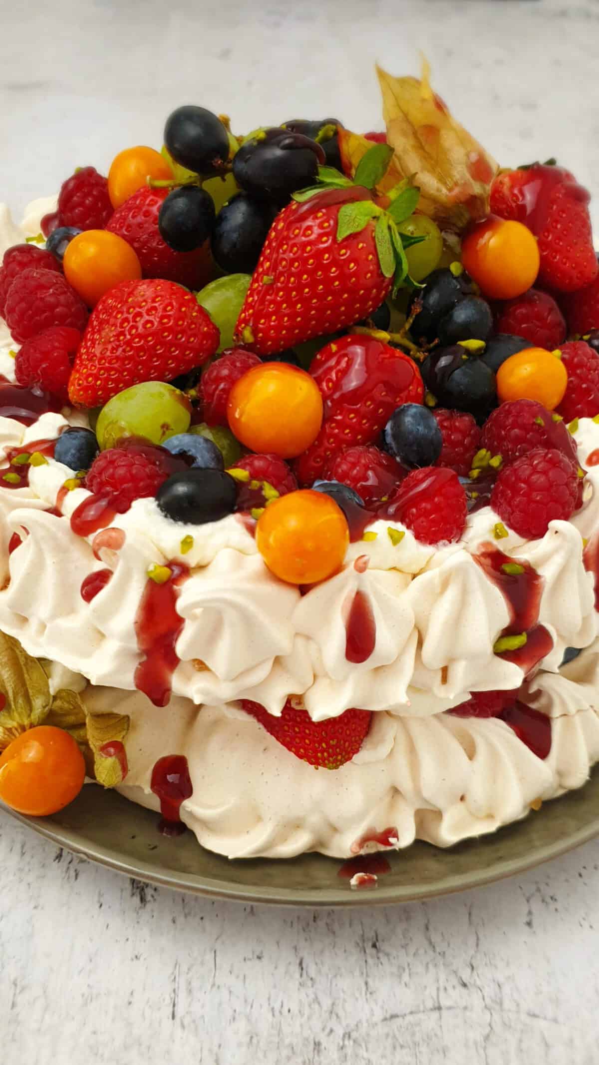 Eine zweischichtige Pavlova Torte mit Sahne Füllung und Früchte Topping auf einem Teller angerichtet.