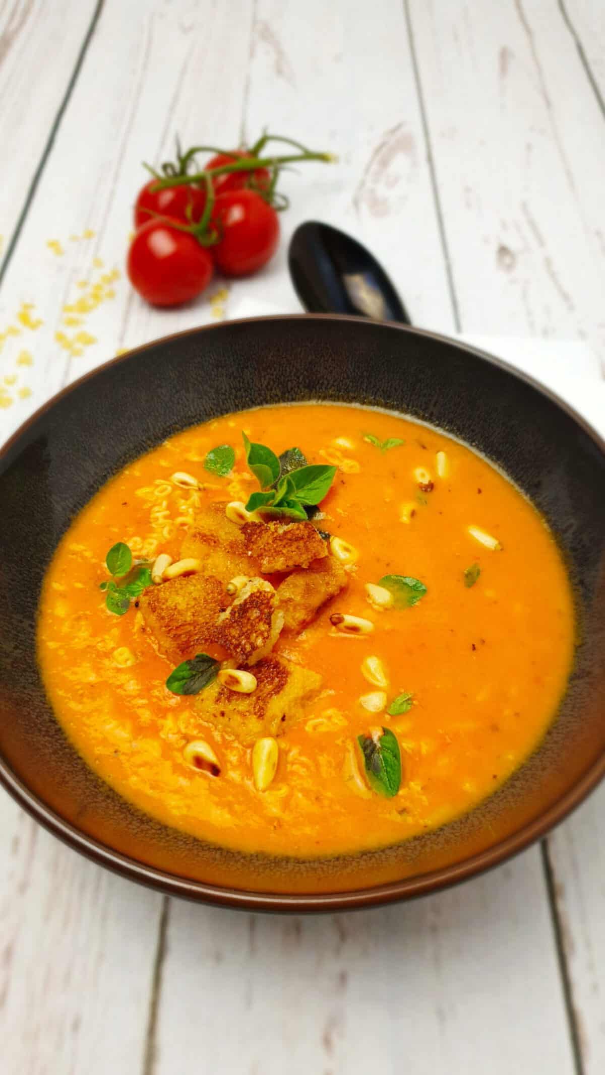 In einer braunen Schale Tomaten-Buchstaben-Suppe mit Croutons und Pinienkernen.