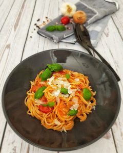 In einer braunen Schale angerichtet Dinkel Spaghetti mit Tomaten-Kokosmilch-Soße. Garniert mit Basilikum Blättern.