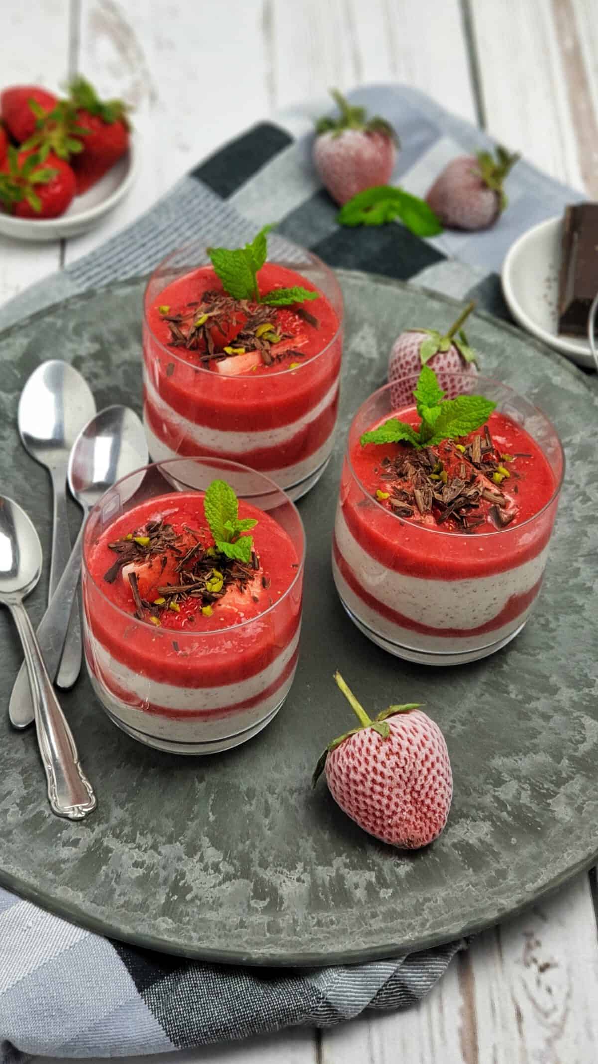 3 Gläser mit Joghurt-Dessert im Glas geschichtet mit Erdbeerpüree. Dekoriert mit Schokolade und frischer Minze.