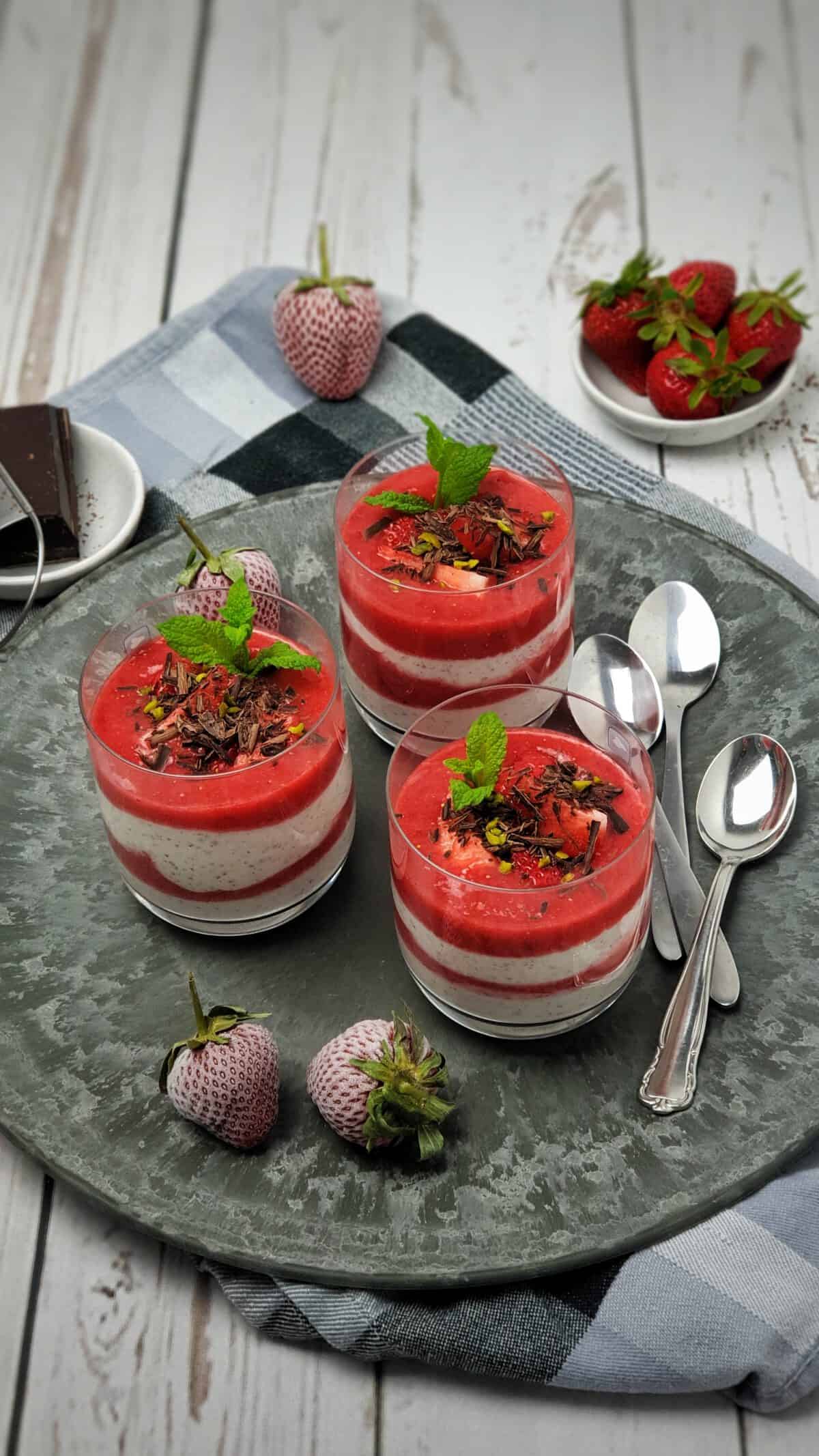 3 Gläser mit Joghurt-Dessert im Glas geschichtet mit Erdbeerpüree. Dekoriert mit Schokolade und frischer Minze.