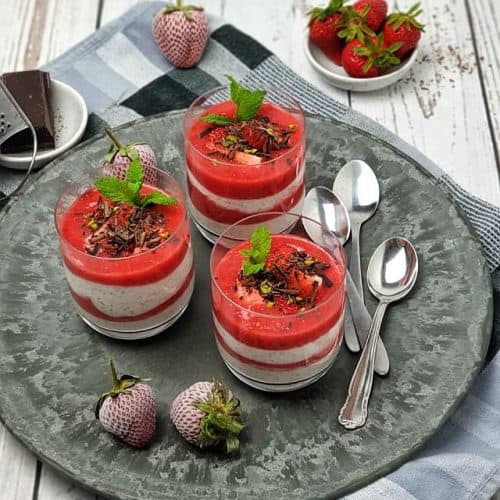 Joghurt-Schicht-Dessert mit Erdbeerpüree im Glas. Dekoriert mit Schokostreusel, gehackten Pistazien und frischen Minzblättern.