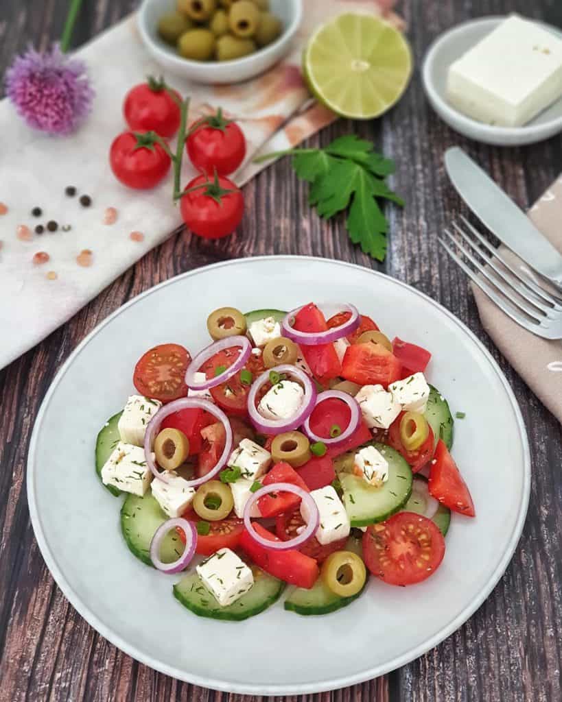 Auf einem hellen Teller angerichteter griechischer Bauernsalat mit Tomaten, Gurken, roten Zwiebeln und Feta.