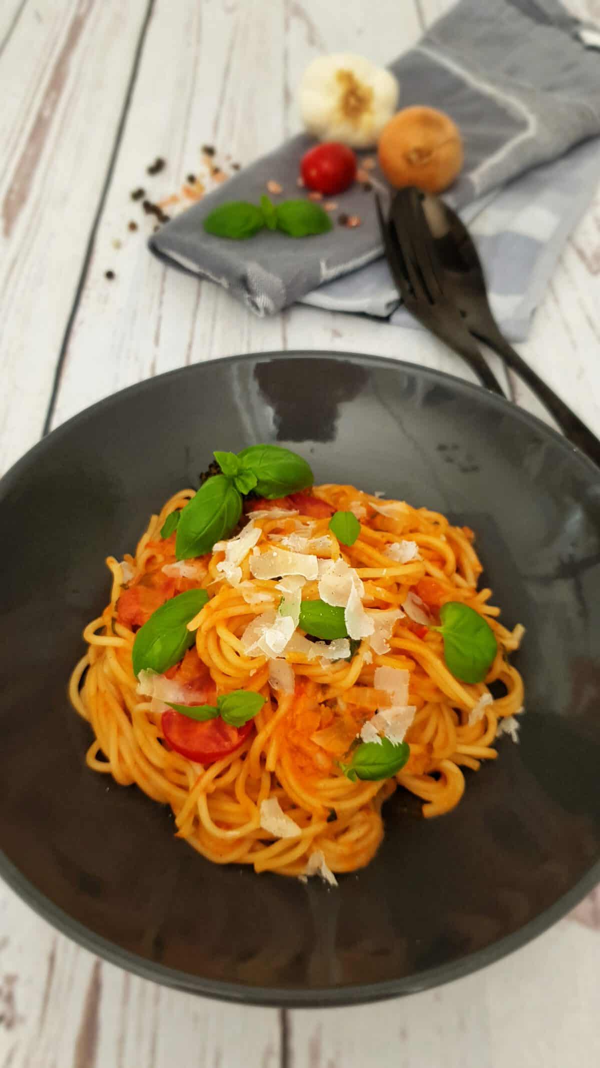 In einer braunen Schale angerichtet Dinkel Spaghetti mit Tomaten-Kokosmilch-Soße. Garniert mit Basilikum Blättern.