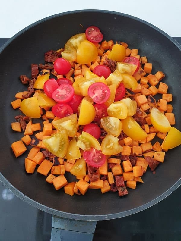 In einer Pfanne angebratene Süßkartoffel Würfel mit geschmorten gelben und roten Tomaten.