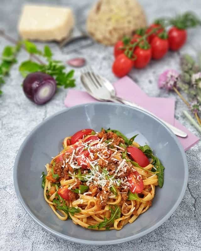 Pasta bella italia mit Hackfleischsoße, Rucola und frischen Tomaten dekarativ angerichtet mit Parmesan bestreut in einer grauen Schale