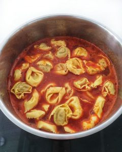 In einem Topf Tortellini in Tomaten-Suppe.