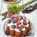 Schoko Waffeln mit Sahne und gefrorenen Beeren dekorativ auf einem Teller angerichtet und fotografiert.Im Hintergrund ein Teller mit gestapelten Waffeln und eine kleines Wildblumensträußchen.