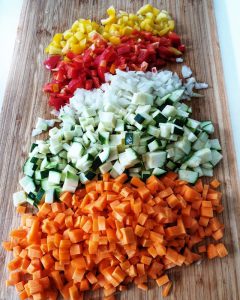 Die Möhren, Zucchini, Zwiebeln und Paprika für das asiatische Reisgericht ist in kleine Würfel geschnitten auf einem Schneidebrett fotografiert.