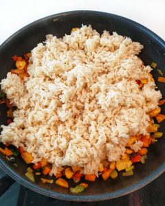 Der vorgekochte Reis kommt zum Fleisch und Gemüse in den Wok