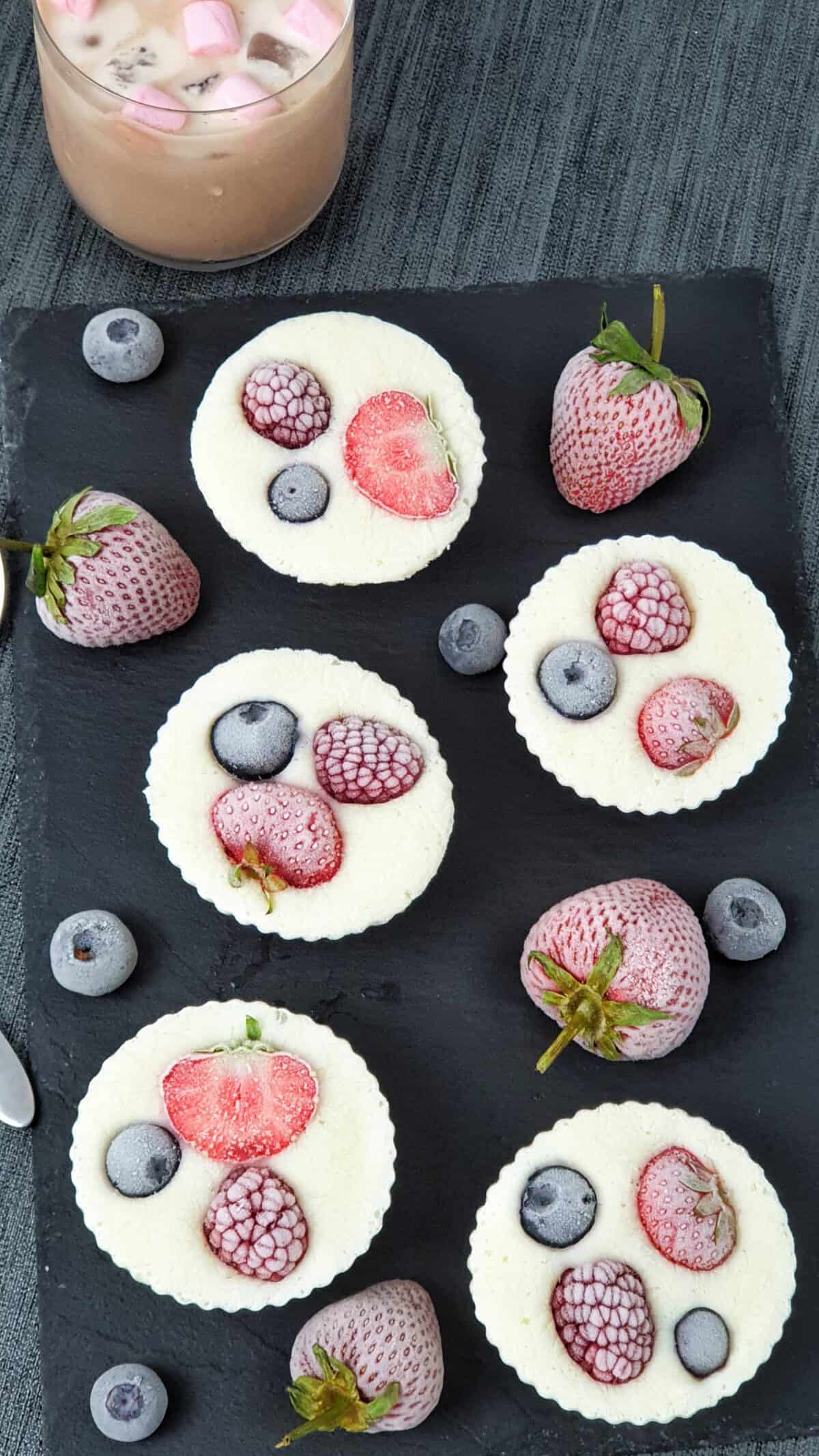 Auf einer Schieferplatte angerichtet Frozen Yoghurt Muffins mit Früchten.