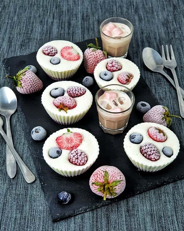 Auf einer Schieferplatte angerichtet Frozen Yoghurt Muffins mit Früchten.