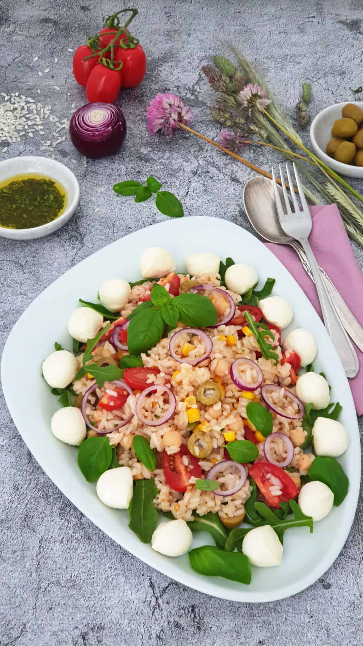 Auf einer weißen Platte angerichtet ein Italienischer Reis-Salat mit Mozzarella und Rucola. Im Hintergrund Deko.
