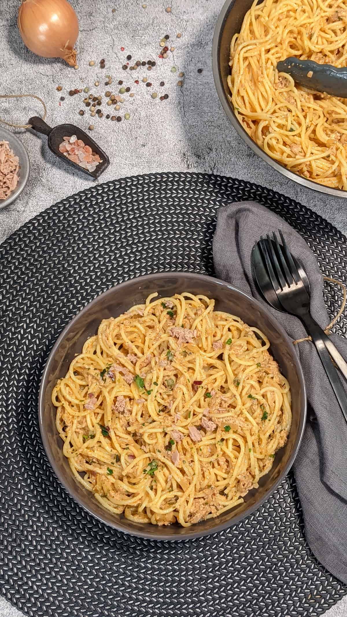 Spaghetti mit Thunfisch-Sahne-Soße angerichtet in einer grauen Schale. Deko drumherum.