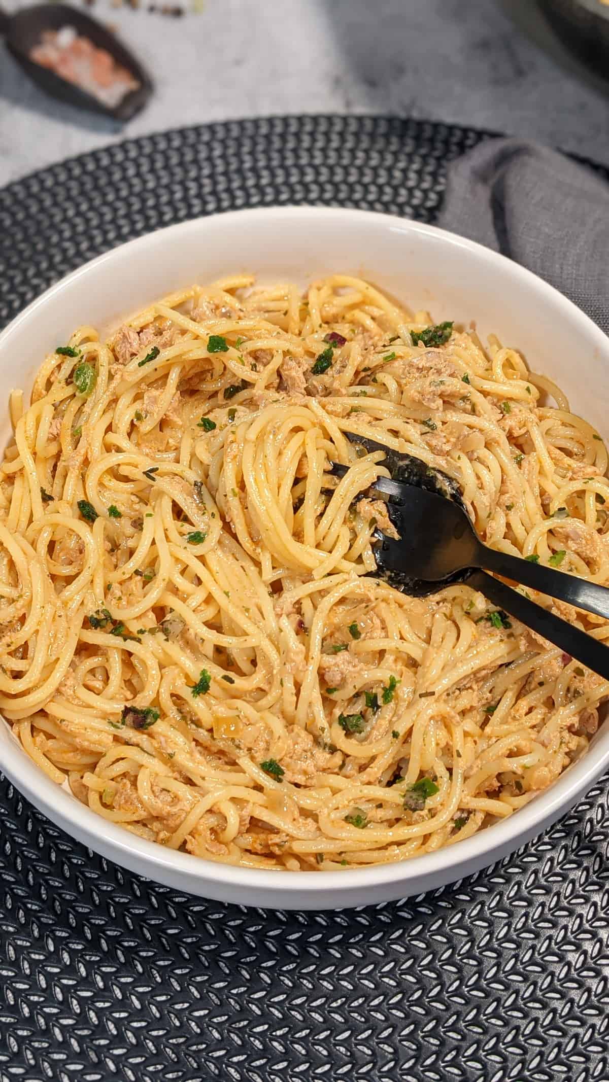 Spaghetti mit Thunfisch-Sahne-Soße angerichtet in einer weißen Schale. Deko drumherum.