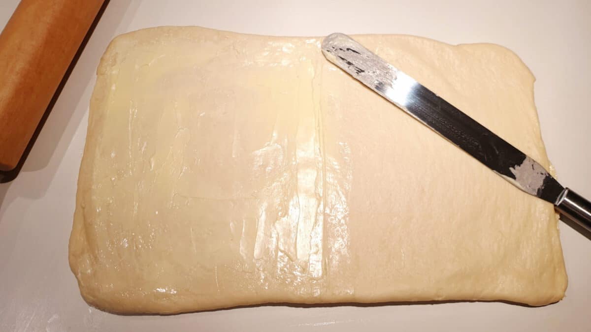 Plunderteig mit Butter bestrichen auf einer Küchenarbeitsplatte.