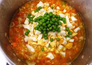 In einem Topf eine rote Suppe mit Möhren, Ei, Nudeln und Erbsen.