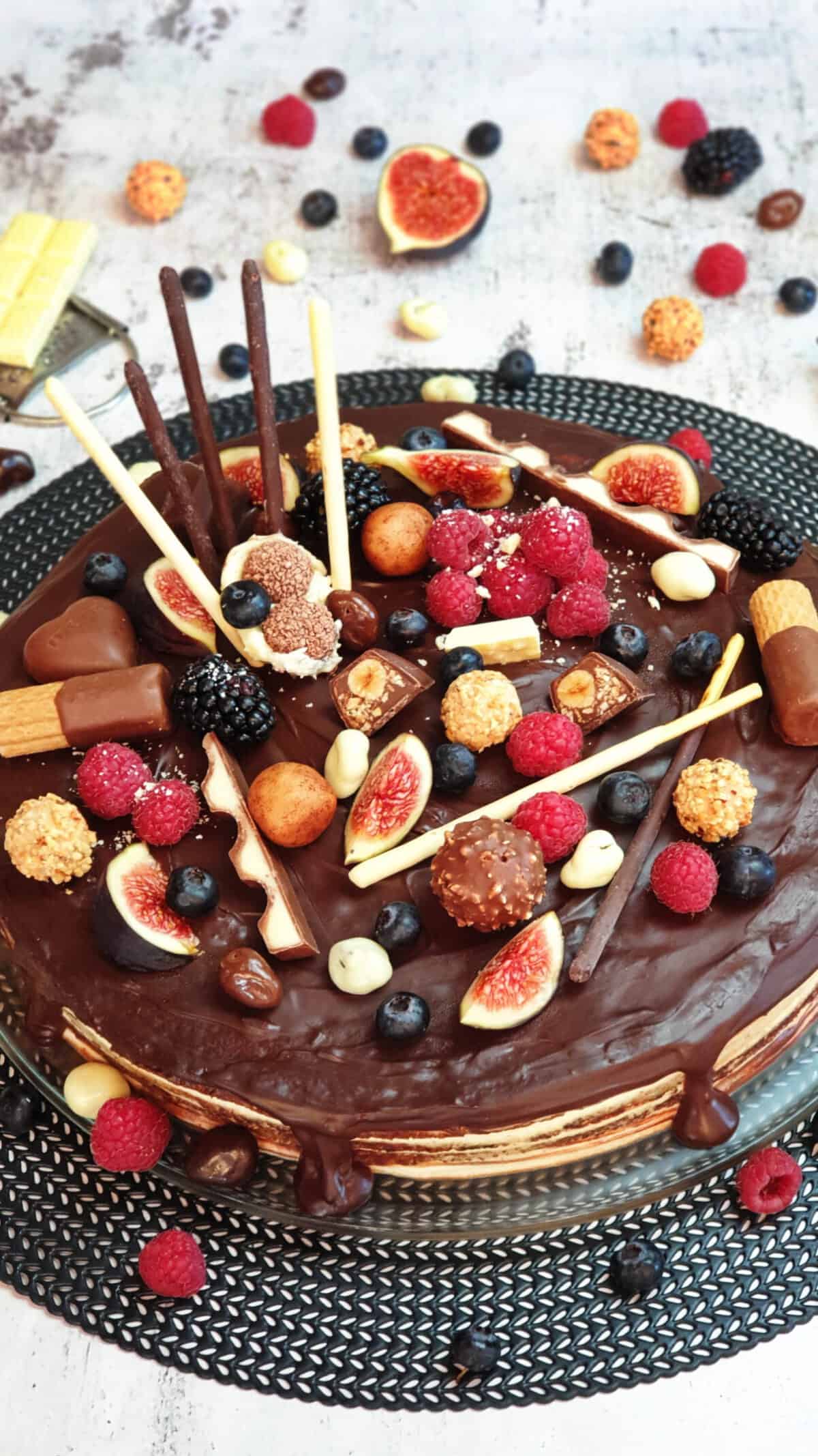 Eine Candy Cake Torte verziert mit Früchten und Schokolade. Im Hintergrund Deko aus Schokoriegeln und Feigen.