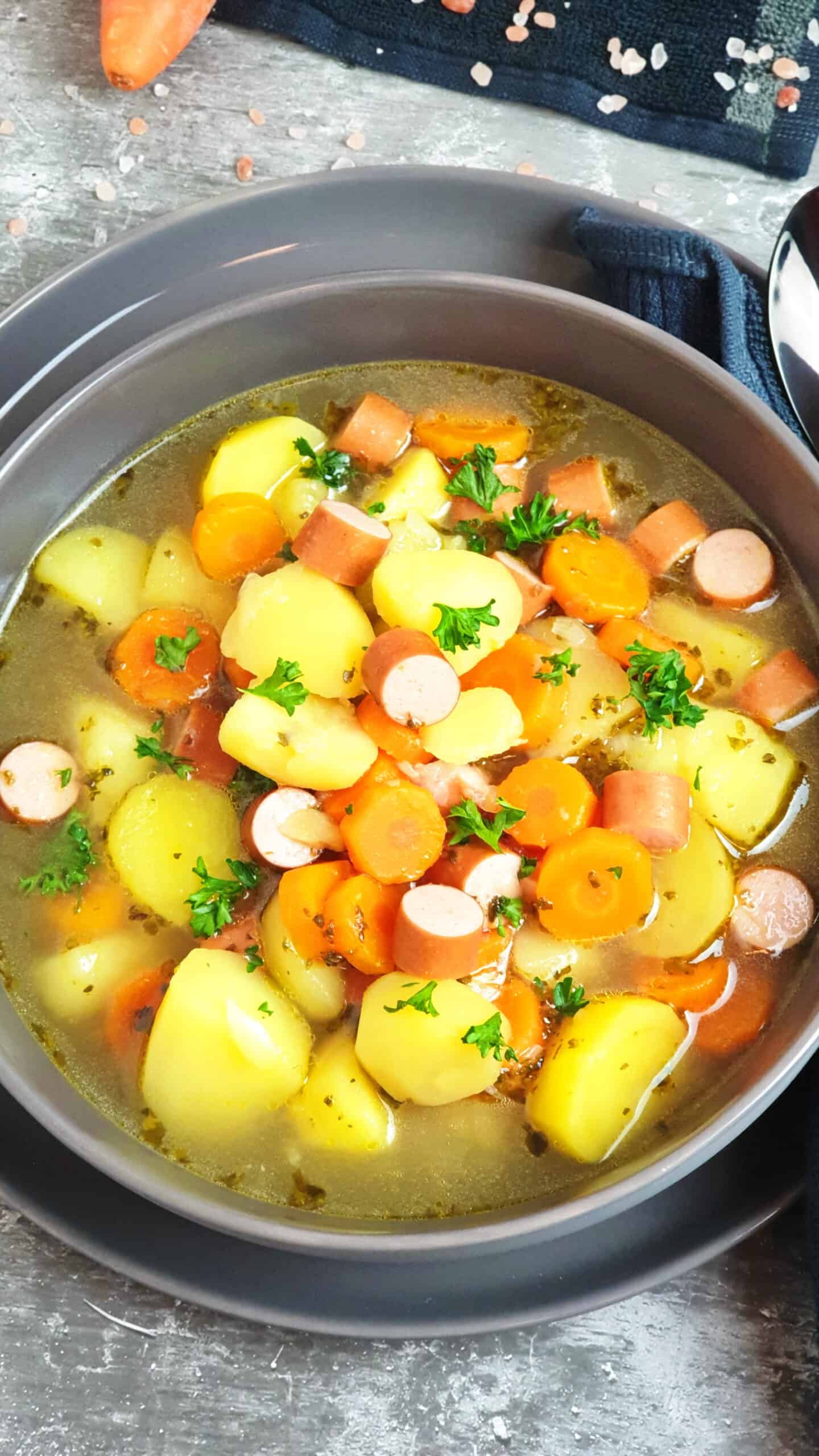 In einer grauen Schale eine Kartoffel-Möhren Suppe mit Wiener Würstchen. Mit Petersilie bestreut. Im Hintergrund Deko. 