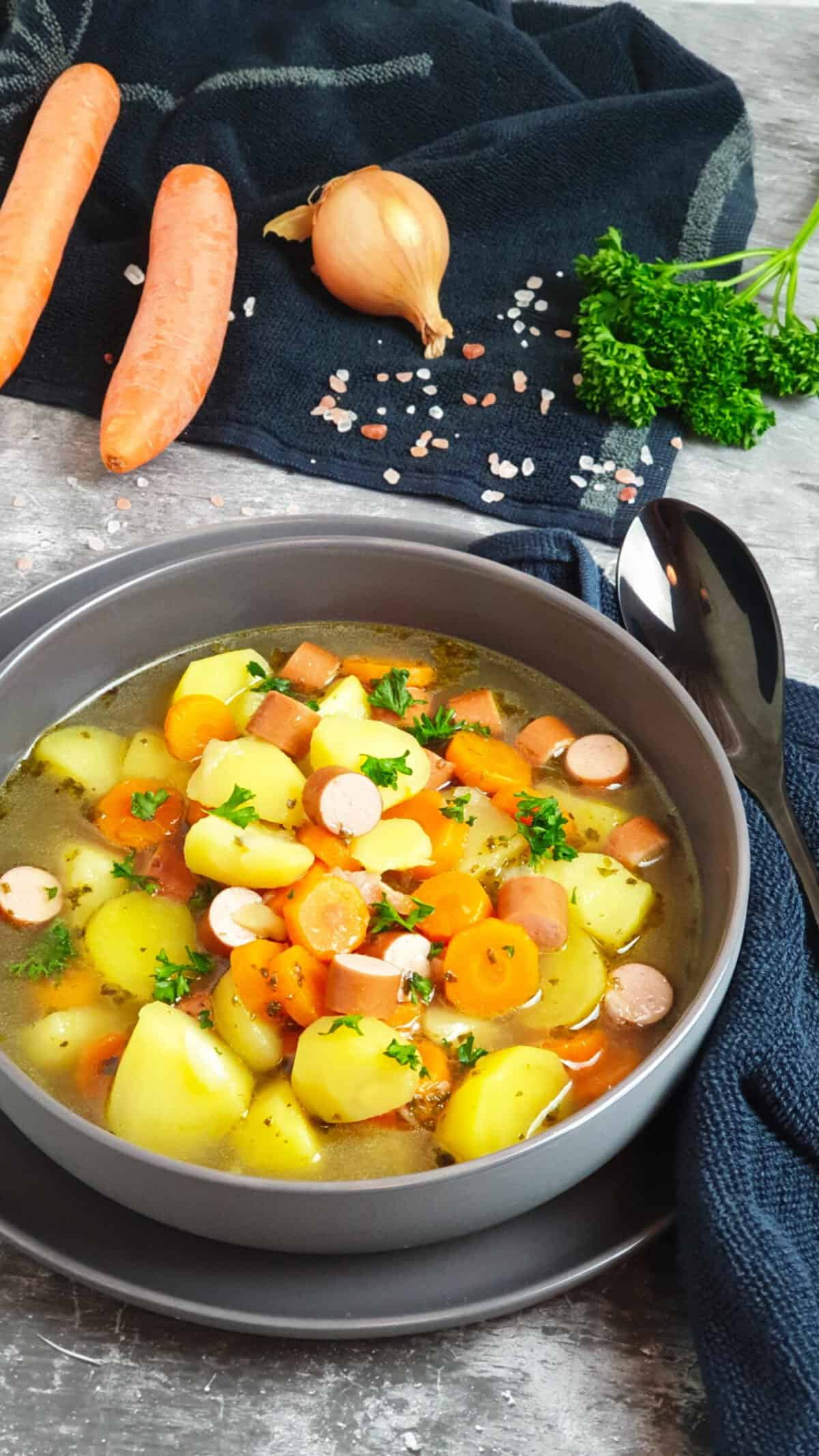 In einer grauen Schale angerichtet Kartoffel Möhren Suppe mit Würstchen. Mit Petersilie bestreut. Im Hintergrund Deko.