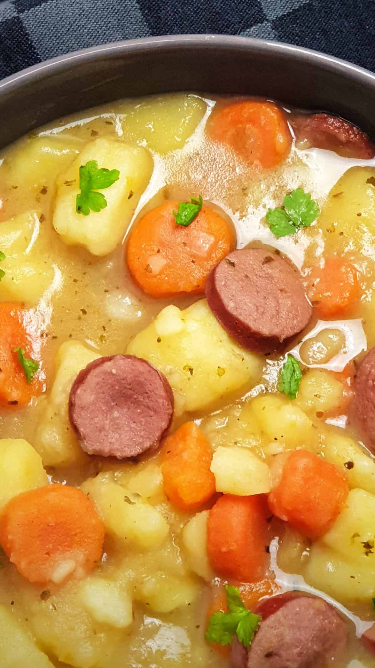 In einer grauen Schale angerichtet ein Kartoffel-Möhren Eintopf mit Rindswurst.