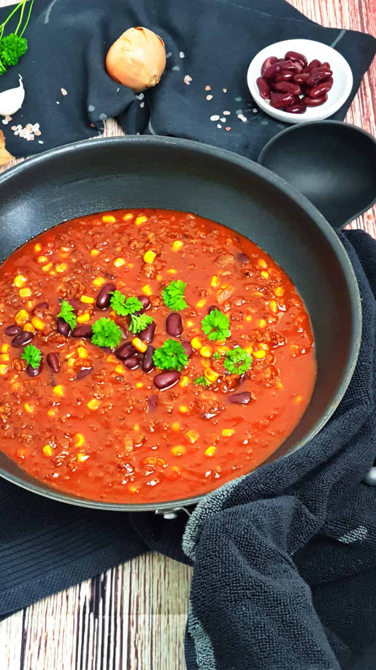 Chili con Carne in mit Hackfleisch, Mais und Bohnen einer schwarzen Pfanne.