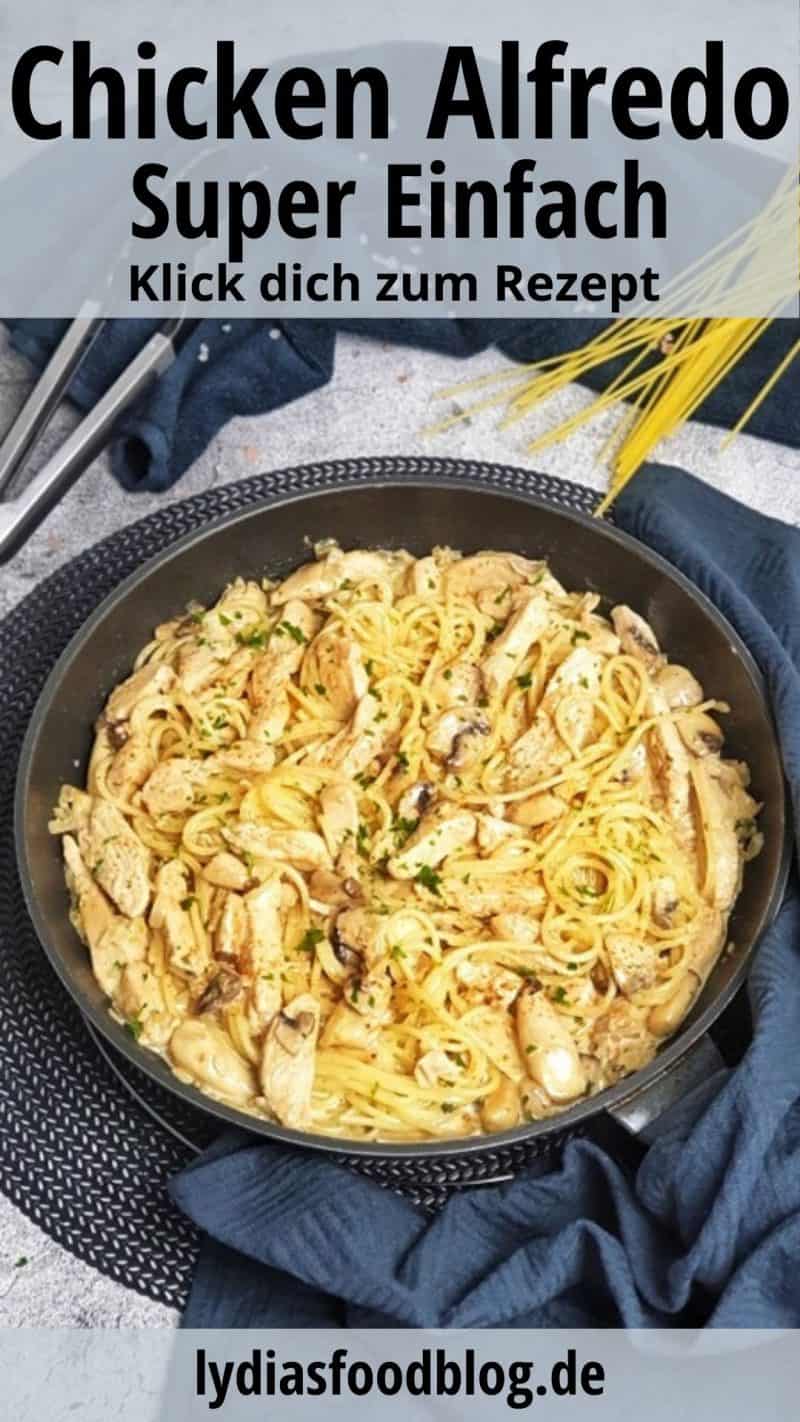 In einer schwarzen Pfanne zu sehen Chicken Alfredo, ein Nudelgericht mit Hähnchenstreifen, Sahne-Soße und Pilzen. Hinter der Pfanne auf einem dunklem Handtuch dekorativ ein paar Spaghetti Nudeln und eine Zange zu sehen.