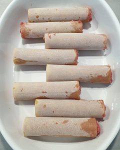 Die gefüllten Cannelloni liegen nebeneinander in der weißen Auflaufform.