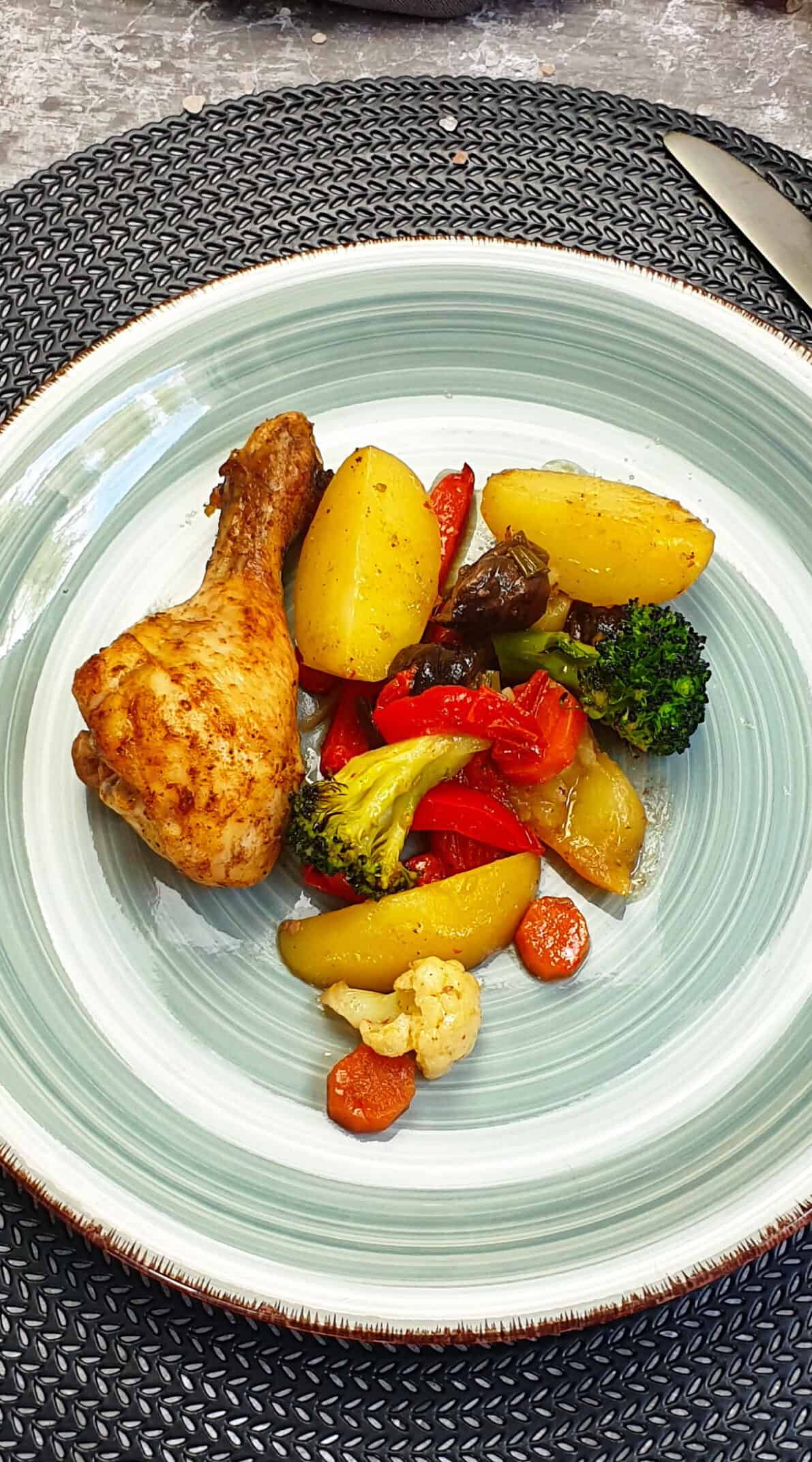 Auf einem türkisfarbenen Teller ein Hähnchenschenkel mit buntem Gemüse und Kartoffeln aus dem Ofen. Im Hintergrund Deko. 
