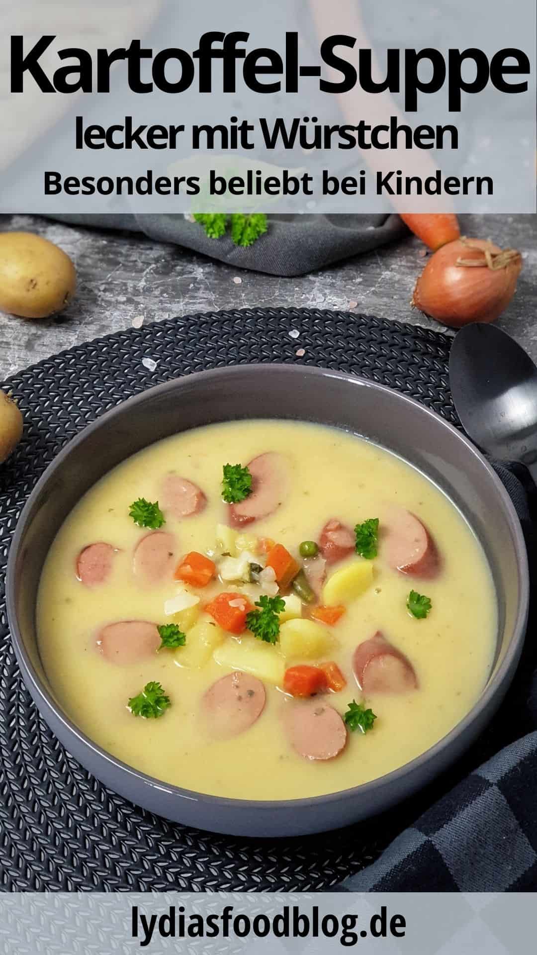 In einer grauen Schale dekorativ angerichtet eine cremige Kartoffelsuppe mit Würstchen sowie Kartoffel und Gemüsestücken. Im Hintergrund auf einem Handtuch liegt ein Baguette, eine Möhre und Kartoffeln.