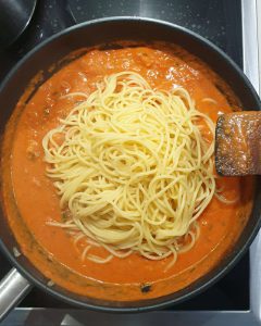 Gekochte Spaghetti in Tomaten-Sahne-Soße in einer Pfanne.