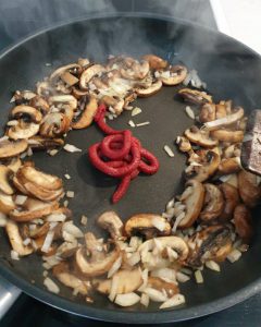 In einer Pfanne angebratene Pilze mit Zwiebeln und Tomatenmark.