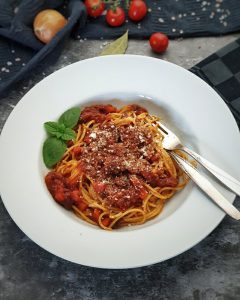 In einem weißen Pasta Teller angerichtet Spaghetti Bolognese mit Parmesan bestreut und einem Baslilikumblatt dekoriert.