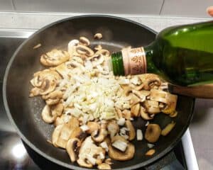 Angebratene Champignons mit Zwiebel Würfel und Öl in einer Pfanne.
